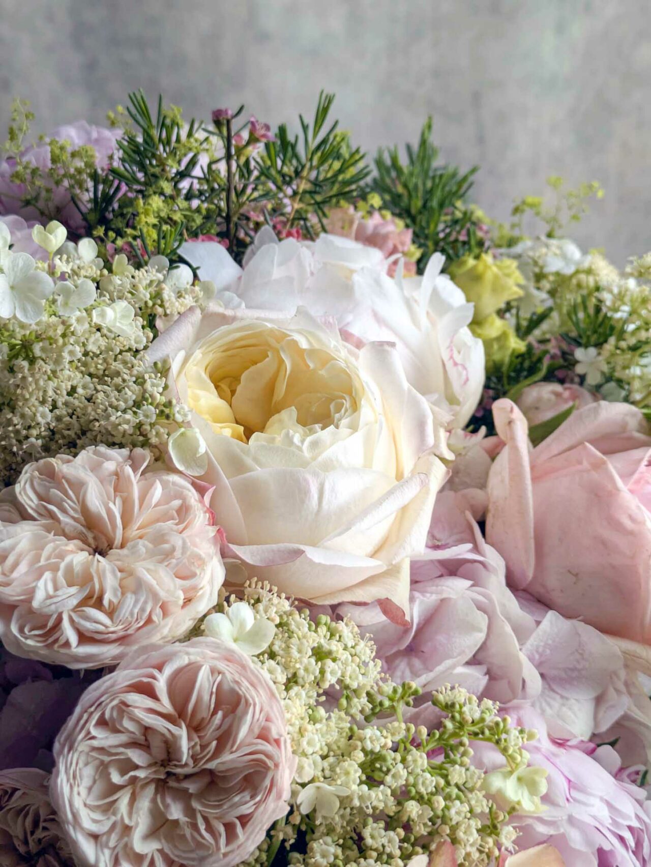 A close-up bouquet of soft pink and cream peonies with delicate greenery and small white blooms.
