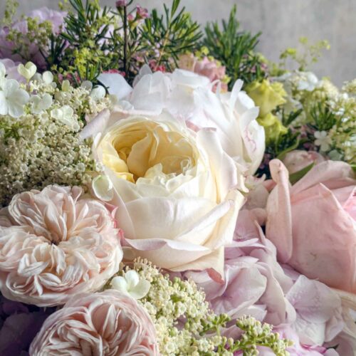 A close-up bouquet of soft pink and cream peonies with delicate greenery and small white blooms.